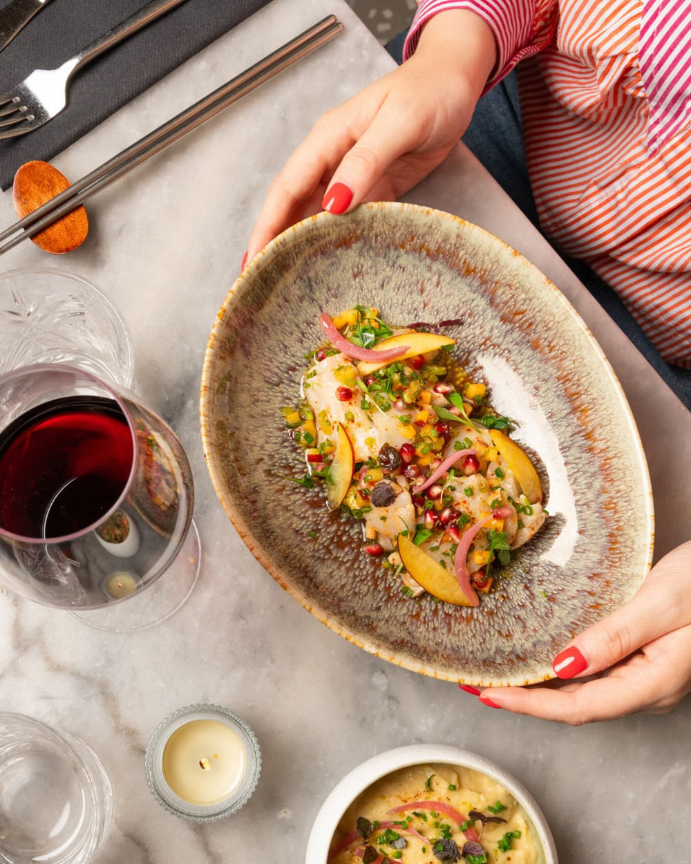Assiette gastronomique tenue par une femme, plat coloré avec grenades et pêches, verre de vin rouge, restaurant Paris